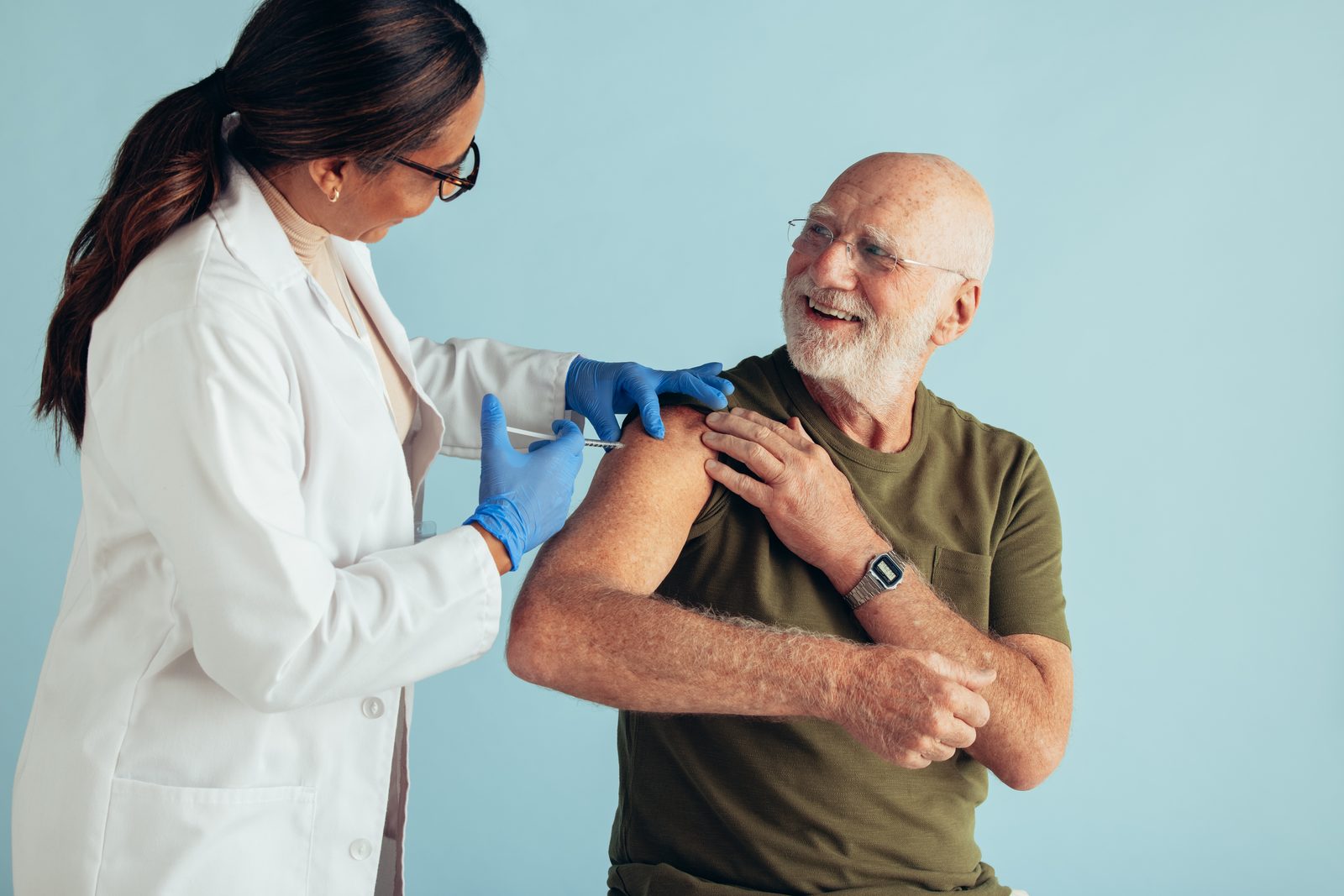 A healthcare provider gives an older man a flu shot in his upper arm