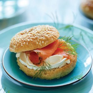 Traditional bagel with cream cheese, smoked salmon and fresh dill served on a blue plate,  close up view.