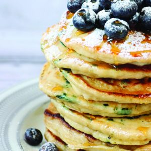 Stock photo showing close-up view of American-style, fluffy blueberry pancake pile topped with fresh berries and drizzled with honey.