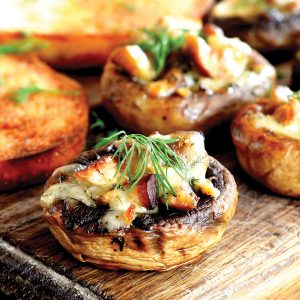 Stuffed mushrooms and fried toasts on a chopping board and wooden table. Baked mushroom caps stuffed with cheese and meat recipe. Closeup